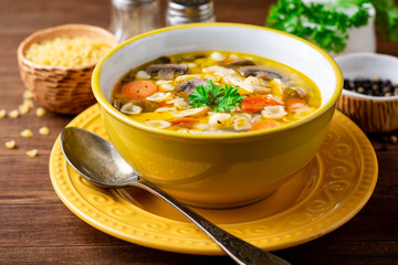 Chicken soup with mushrooms, vegetables and pasta in bowl on wooden table.