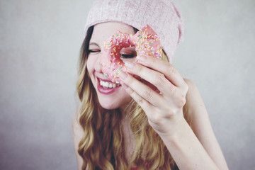 Retrato divertido de una mujer joven y rubia con un donut rosa 