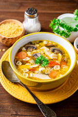 Chicken soup with mushrooms, vegetables and pasta in bowl on wooden table.