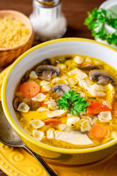 Chicken soup with mushrooms, vegetables and pasta in bowl on wooden table.