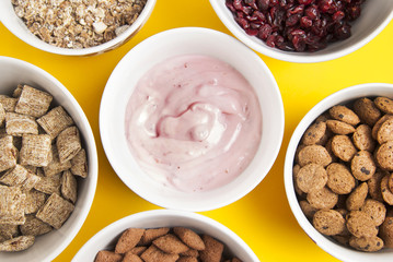 Bowls of mix whole grain muesli, dried fruits, granola and oatmeals arranged in circle. Isolated on yellow background. Top view.
