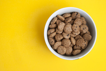 Breakfast corn chocolate pils in white round bowl. Delicious breakfast. Isolated over yellow background. Top view.