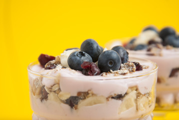 Close up breakfast in glass cup. Granola oat meals, with dried fruits, blueberries and yogurt. Isolaed on yellow background.