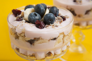 Close up breakfast in glass cup. Granola oat meals, with dried fruits, blueberries and yogurt. Isolaed on yellow background.