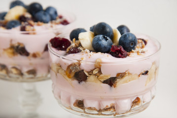 Two glass cup, with granola oat meals, with dried fruits, blueberries and yogurt. Isolated on chopping marble board over white background.