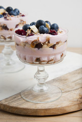 One glass cup, with granola oat meals, with dried fruits, blueberries and yogurt. Isolated on chopping marble board over white background.