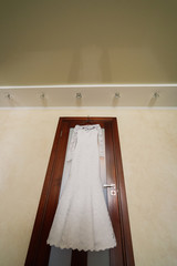 Wedding dress hanging on a wooden door in a bright room.