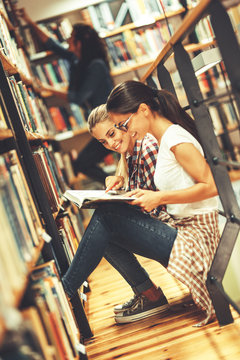 Two female students read and learns by the book shelf at the city library.Reading a book.