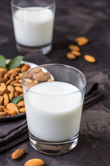Almond milk in glass and almonds nuts on a dark background