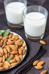Almond milk in glass and almonds nuts on a dark background