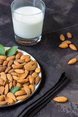 Almond milk in glass and almonds nuts on a dark background