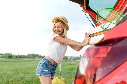 Happy girl pushes suitcases into the trunk of a red car going on a journey