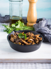 Turkey meat stew with champignon mushrooms and spices served in cast iron skillet on white wooden board