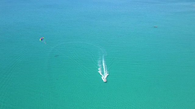 Parasail flying over blue sea pulled boat aerial view. Parasailing over blue sea drone view. Summer activity and extreme entertainment while resting on resort beach.
