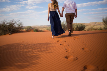A pretty couple walks hand in hand on the red sand dunes in the kalahari region of south africa - obrazy, fototapety, plakaty