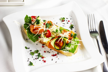 Bruschetta with salmon red fish, fresh vegetables and herbs on a white plate