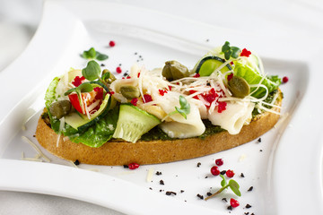 Bruschetta with pesto sauce, fish, fresh vegetables, capers and caviar on white plate