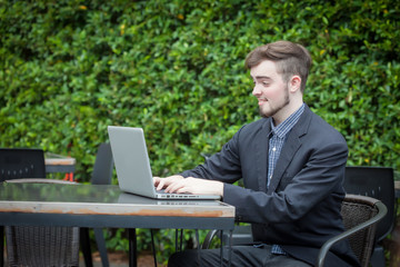 Portrait of young businessman using laptop in modern coffee shop outdoor