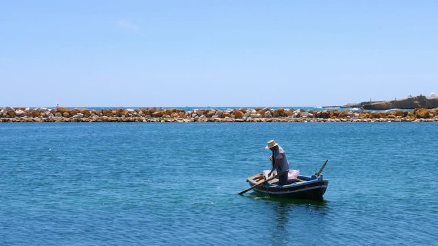Male fisher in boat taking out anchor from sea water