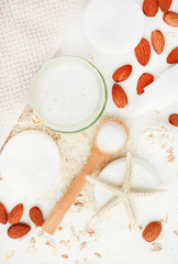 Homemade healing skincare lotion recipe with rice water and almond milk. Facial cleanser liquid soap in jar with nuts and oat flakes ingredients on white table preparation, vertical.