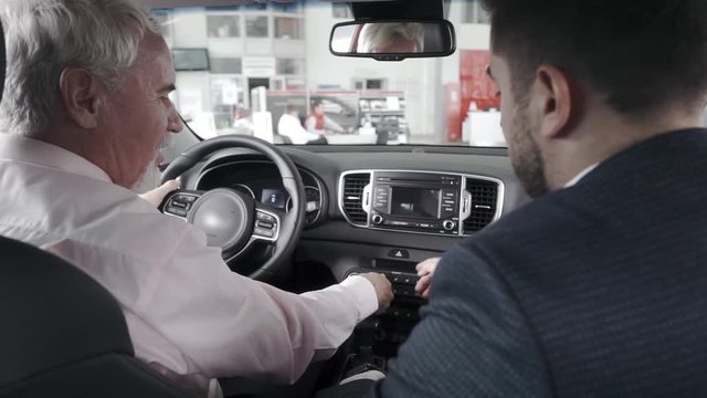 Client is asking a sales man question, sitting at the stearing wheel, checking the quality of the salon.