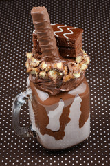 Chocolate extreme milkshake with brownie cake, chocolate paste and sweets. Crazy freakshake food trend. Copy space