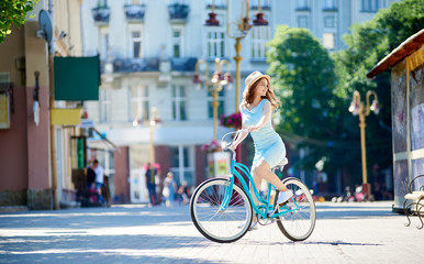 Young woman in a dress and a hat looking around while cycling in the city center copyspace...