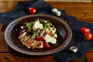 Caesar salad with chicken, parmesan and cherry on a wooden table