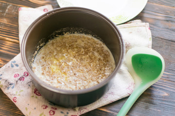 Oatmeal porridge cooked on milk in a saucepan on a dark wooden background.