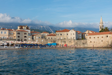Fototapeta na wymiar People are relaxing on the beach near the old city in the popular resort of Budva, Montenegro
