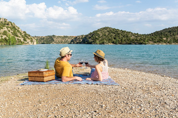 Pareja joven haciendo un romántico picnic cerca de un lago al atardecer