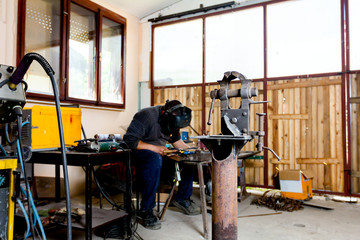 Mechanical hand vise with parallel jaws in the metalwork, craftsman welding in background
