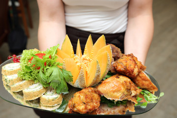 Pięknie udekorowane mięso z kurczaka, warzywa i owoce na tacy trzymanej przez kelnerkę w restauracji.
