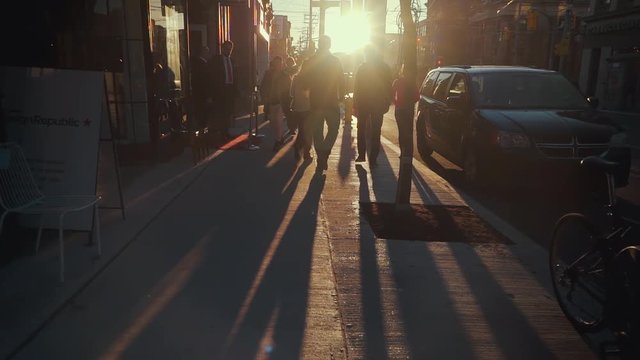 Beautiful evening sunlight shines into the lens as the camera passes through crowds of pedestrians in Toronto