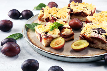 Rustic plum cake on wooden background with plums around.