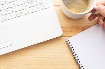 Vista superior de un teclado de un portátil blanco, bloc de notas con espacio para texto y una mano de hombre cogiendo una taza de café. Flat-lay
