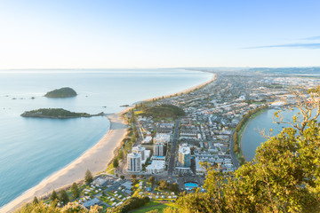 Mount Maunganui stretches out below as sun rises on horizon and falls across ocean beach and buildings