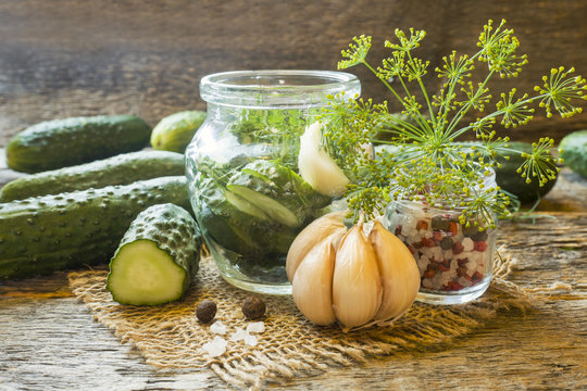 Pickled cucumbers, garlic and spices for pickling in a jar on a wooden table.