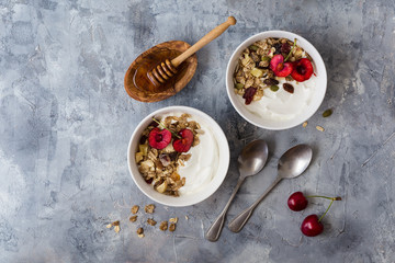 Two bowls with greek yogurt, honey, muesli and cherries on gray stone background. 