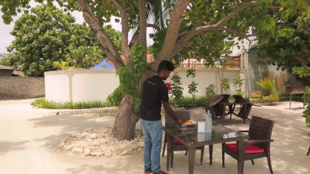 Outdoor restaurant on Dhangethi Island, Maldives. Young waiter serving food. Food and drink concept. 