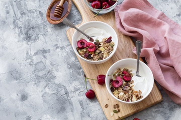 Two bowls with greek yogurt, honey, muesli and cherries on brown stone background. 