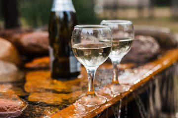 Love, romance, holiday, celebration concept. Bottle and glasses of champagne chilled by waterfall in summer forest on sunset.