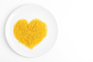 Close up of short and thin dry Italian vermicelli heart. Yellow raw or fresca wheat pasta heart shaped on whit plate on white background. Love pasta concept, free copy space for text