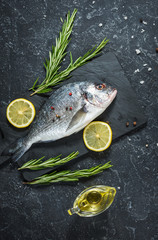 Raw fresh dorado with lemon on dark stone background.