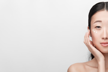 Close up beauty portrait of beautiful asian half naked woman applying face cream isolated on white...