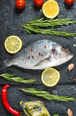 Raw fresh dorado with lemon on dark stone background.