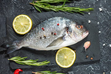 Raw fresh dorado with lemon on dark stone background.