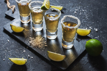 Mexican gold tequila with lime and salt on black stone background.