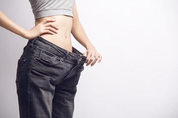 A close-up of a slim girl in a gray tank-top holding her big size jeans on her waist with one hand. Diet. Fitness. 