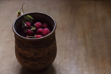 juicy sweet berries of homemade raspberries in a mug on a dark background